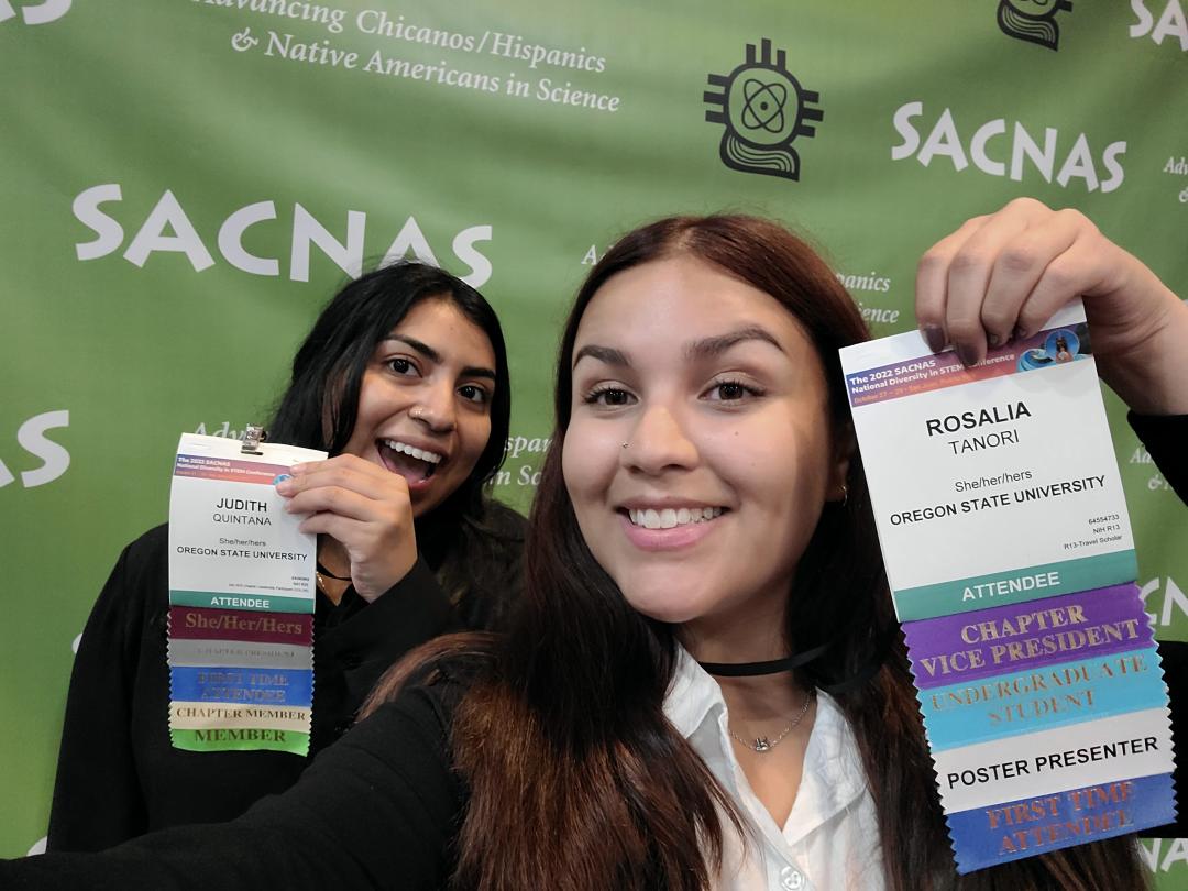 Two women in professional attire pose with name tags at SACNAS conference.