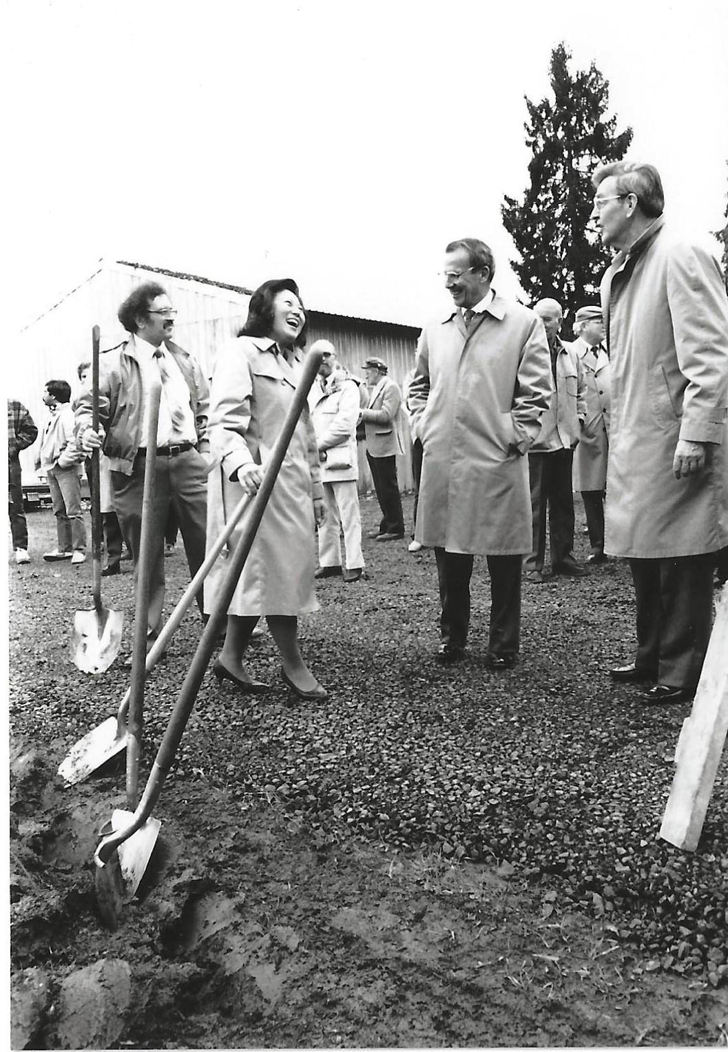Four faculty members outside digging with shovels while smiling and laughing.