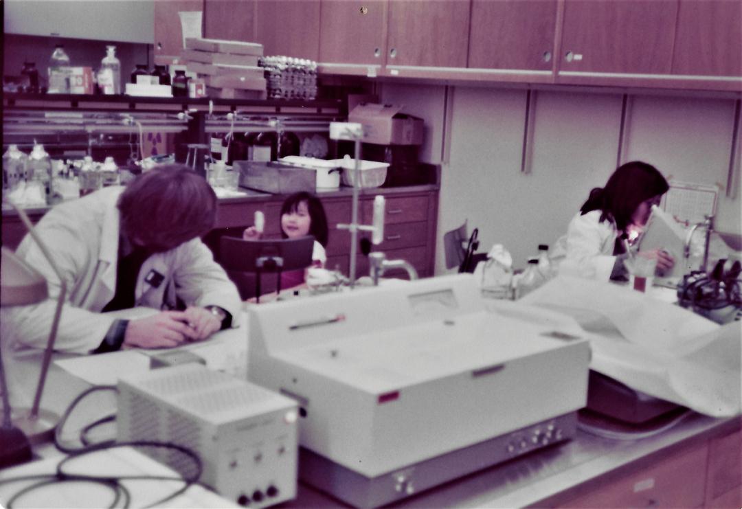 Two graduate students processing placentas with a little girl (Leong's daughter) using microscopes and other lab equipment.