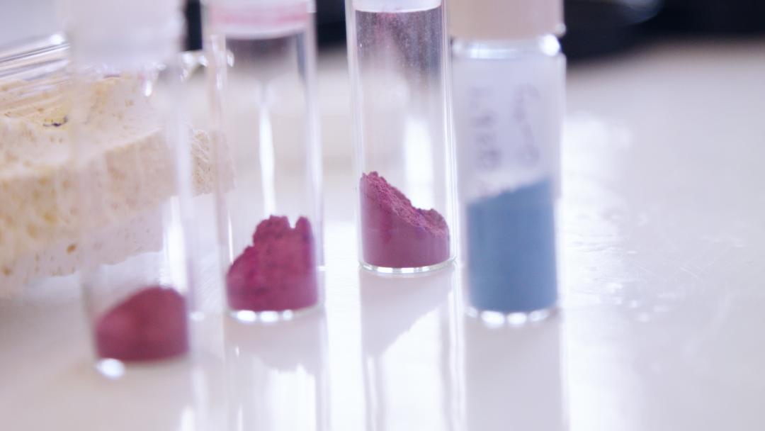 Vials of maroon and blue pigments sit on a desk.