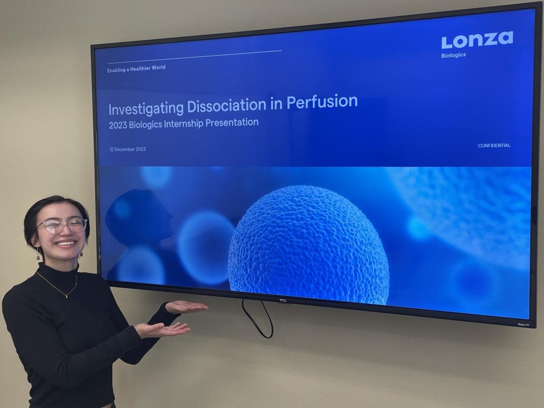 A woman stands in front of a blue science poster. 