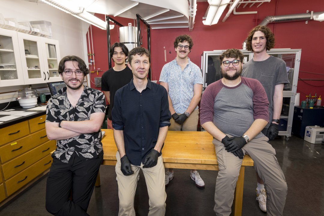 Six men pose for a group picture in a laboratory. 