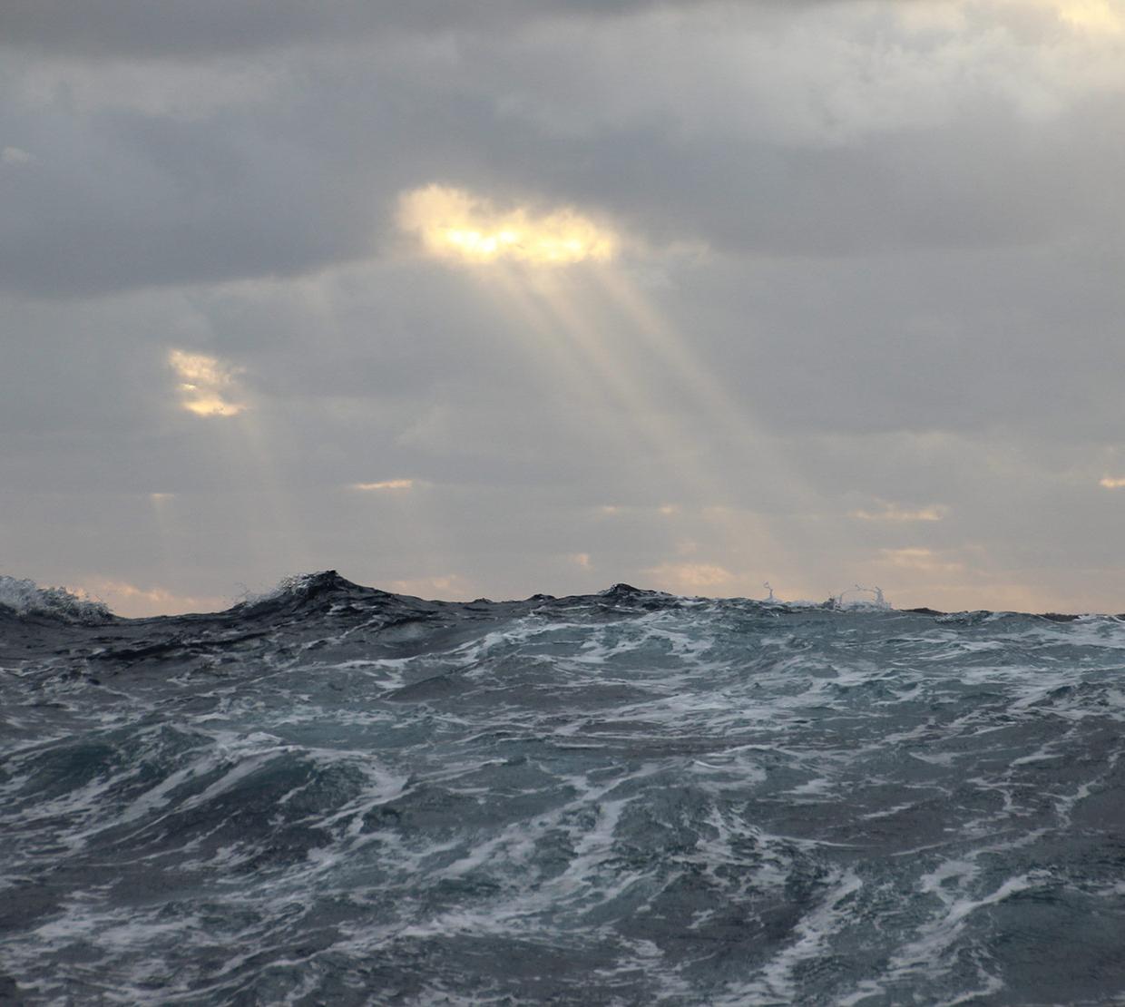 Ocean waves on a dimly lit day with the sun peering through the clouds.