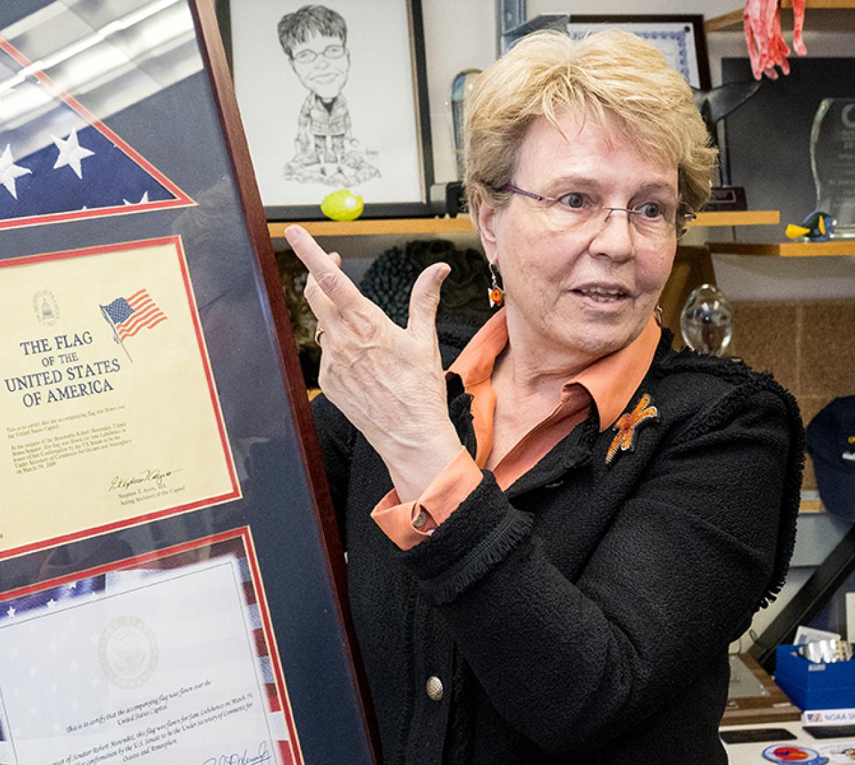 Jane Lubchenco stands in a suit referencing her framed United States flag
