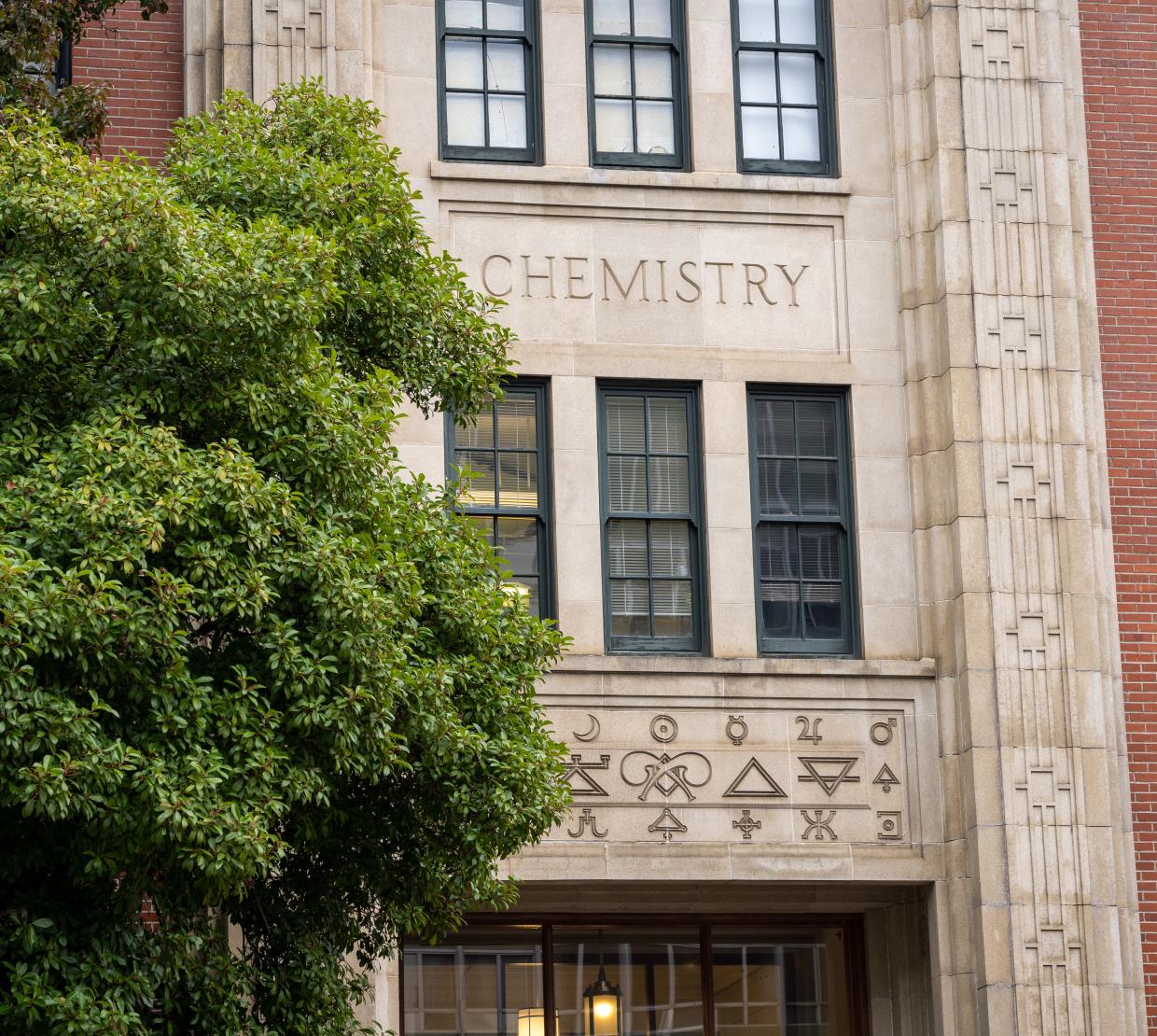 A brick building with the word "chemistry" stands behind a green tree.