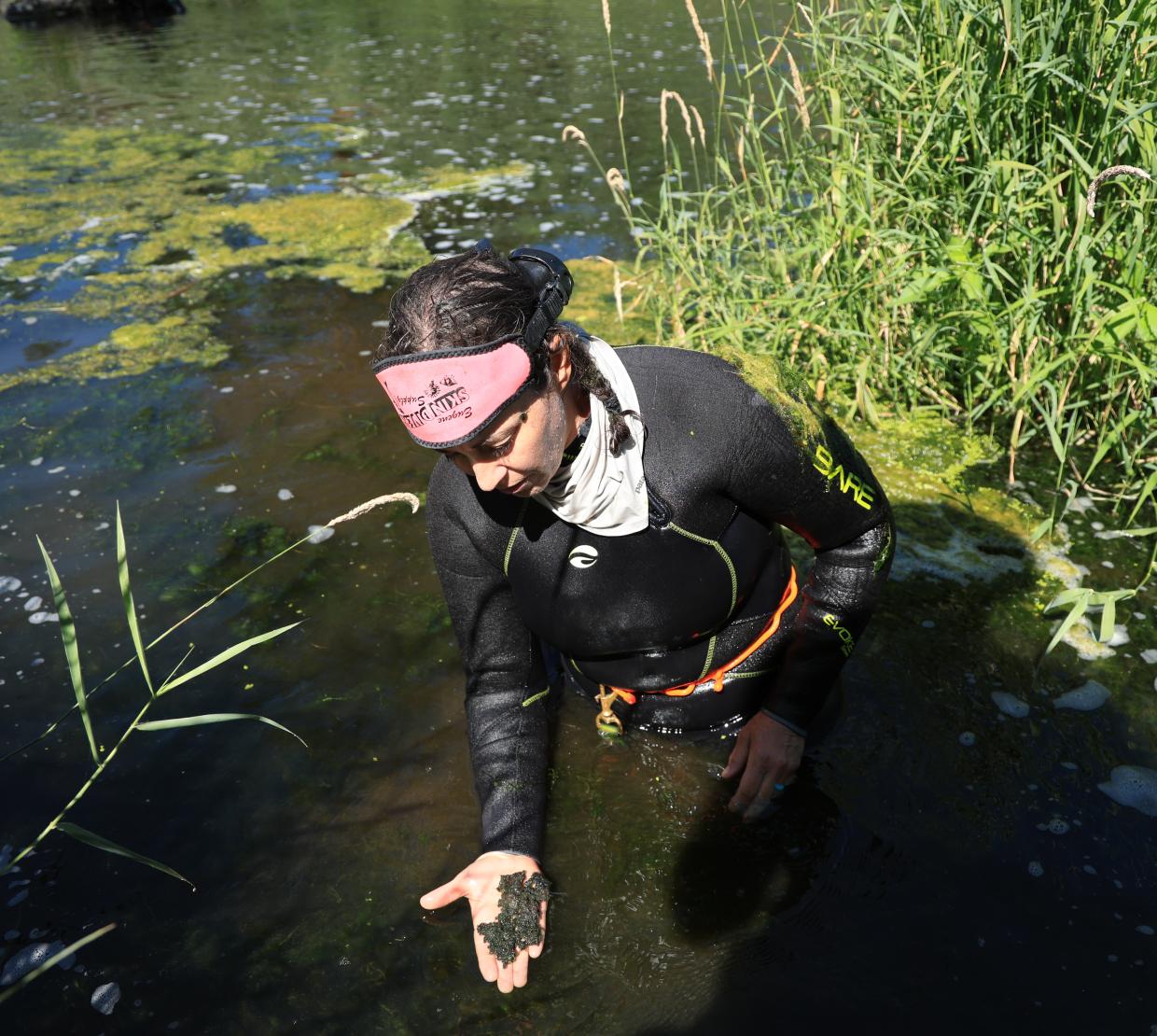 A woman in a stream holds dirt in her hands.