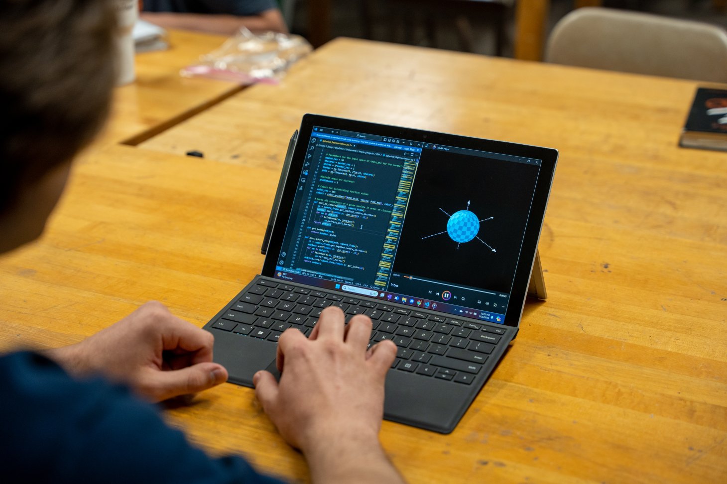 Takach steps through a Python program that runs a video simulation. A blue sphere with arrows pointing out of it is displayed on the computer screen.