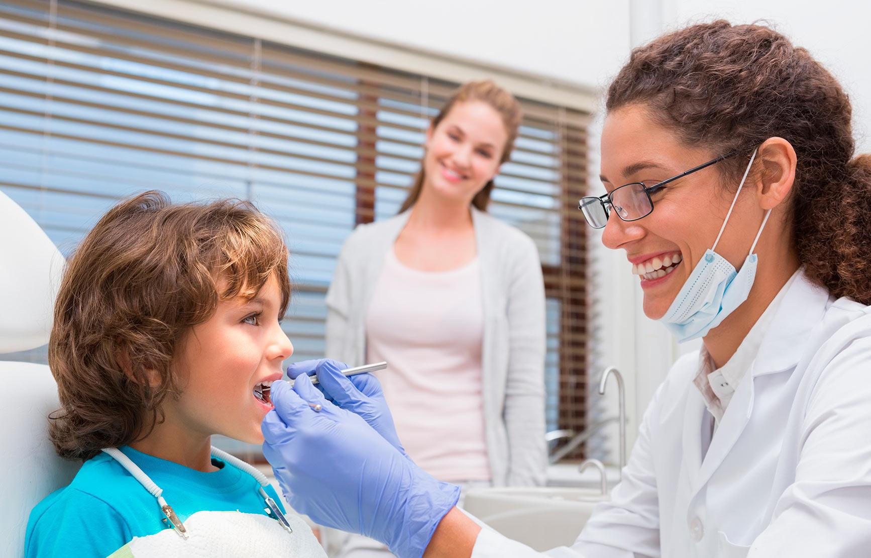 Dentist working on child's mouth next to mother.