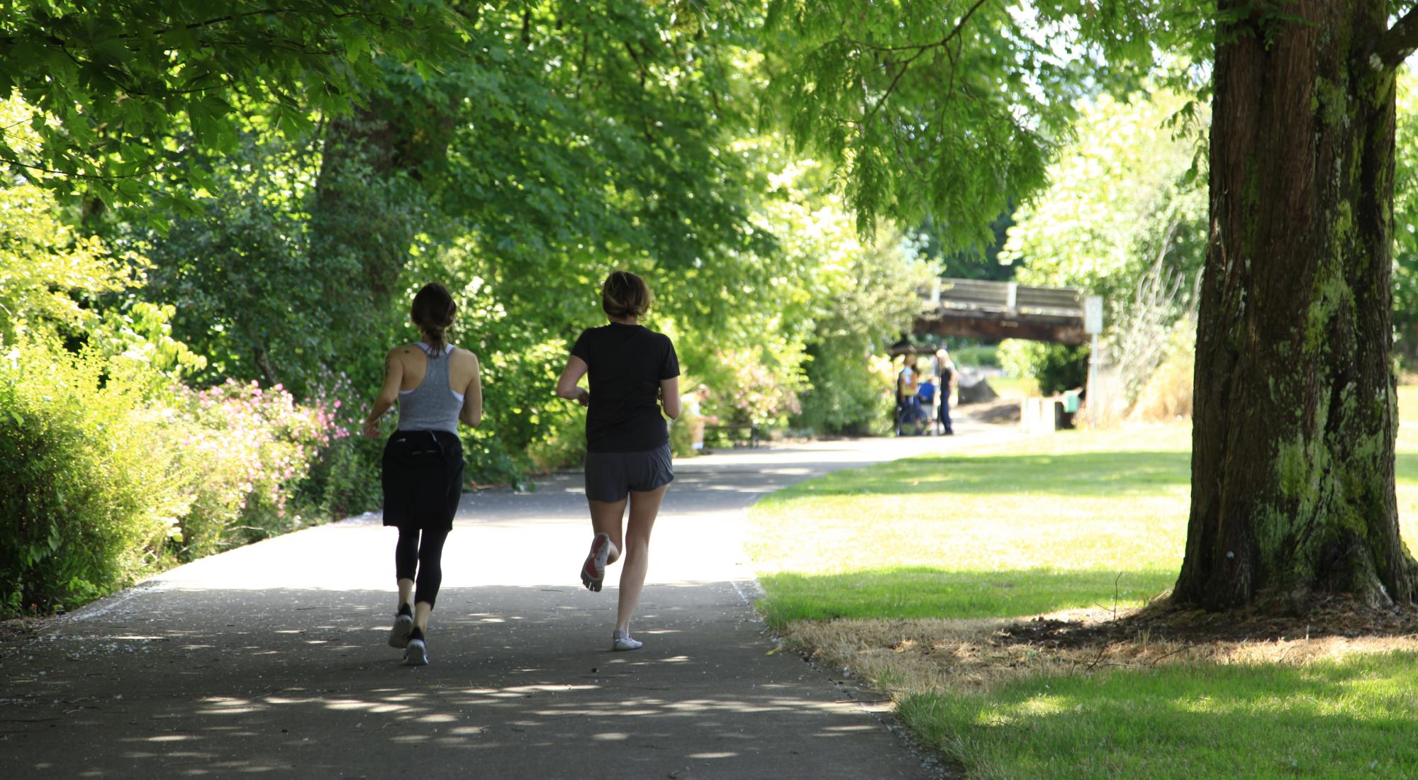 Two women running in downtown Corvallis, surrounded by lush trees