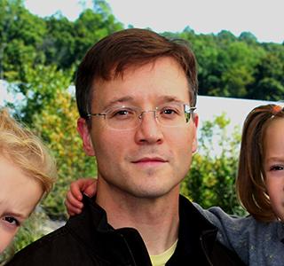 Justin Hall in garden holding daughters in arms