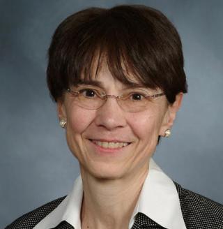 Woman with short brown hair and glasses smiling in front of a gray background