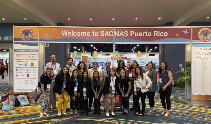 A group of individuals stands in front of an orange SACNAS Puerto Rico banner.