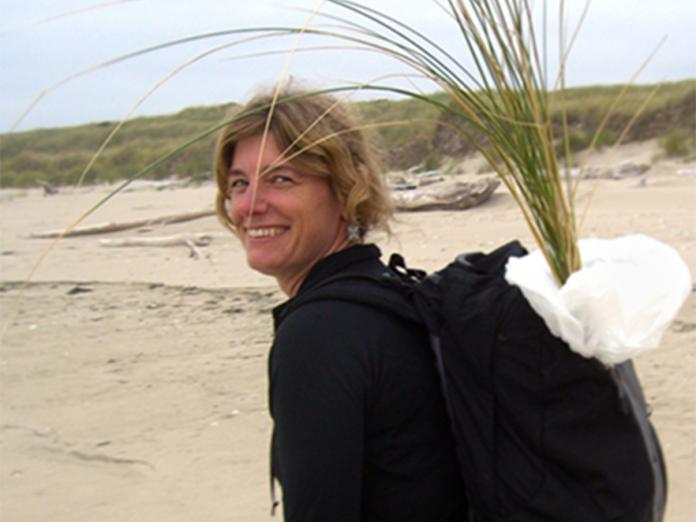 Sally Hacker walking along beach with grass samples in backpack