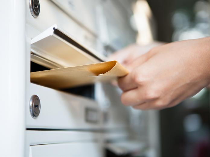 A closeup of a hand dropping an envelope into a mail slot in a facility.
