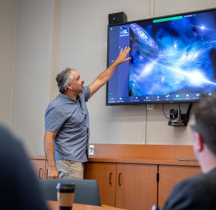 Jeff Hazboun stands in front of a computer screen on a wall looking at gravitational waves.